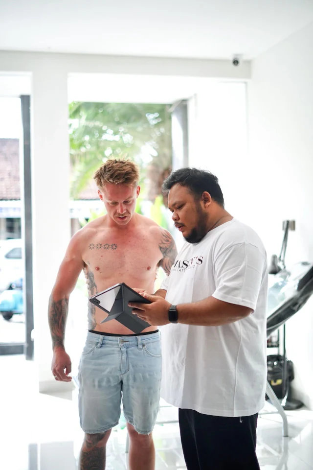 Tattoo artist planning a new design on a tablet with a heavily tattooed client at Mason's Ink