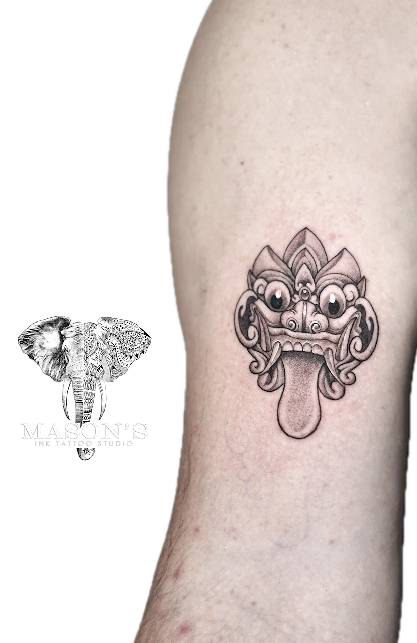 Barong Tattoo Design: a detailed mask tattoo with leaf-like elements on the upper arm