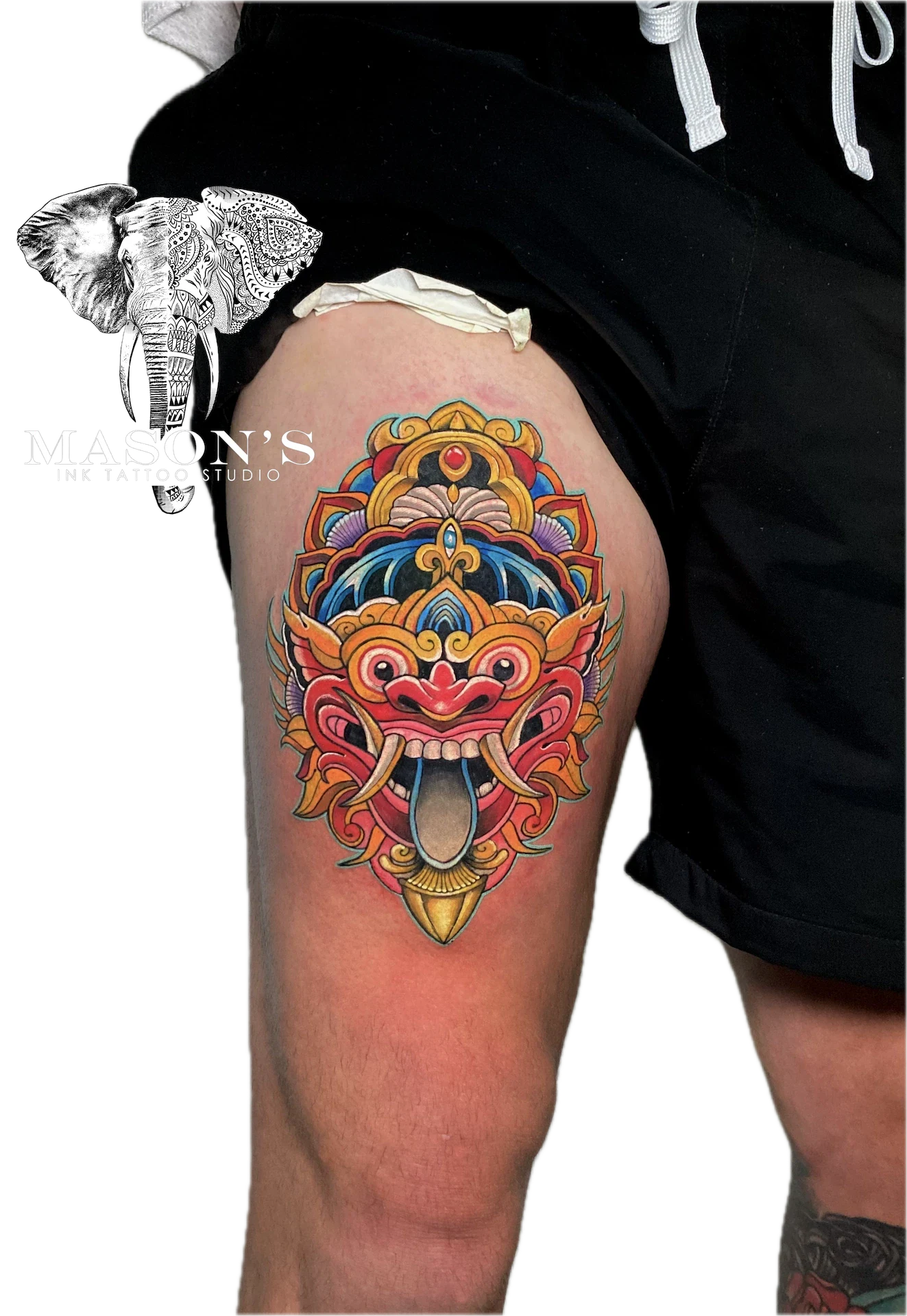 Colored Barong Tattoo Design: a colorful mandala with a mythological mask on a thigh