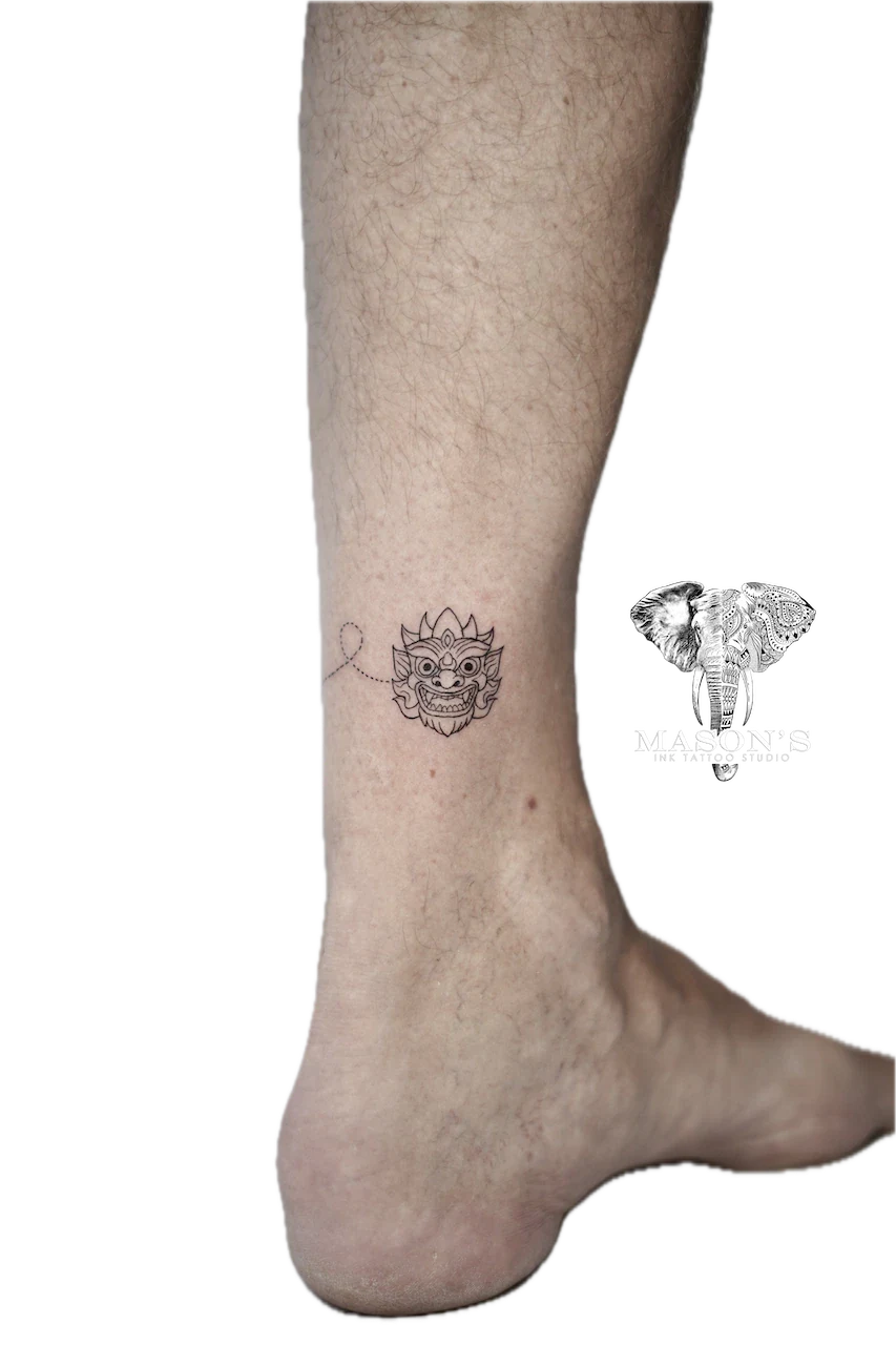 Barong Tattoo Design: Small black and grey mythological mask with heart on calf