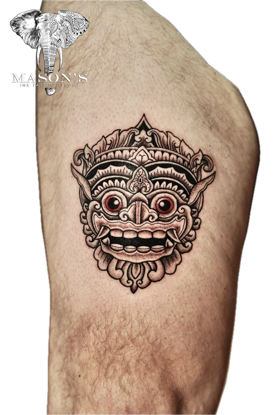 Barong Tattoo Design: a detailed mythological mask with red eyes on the upper arm
