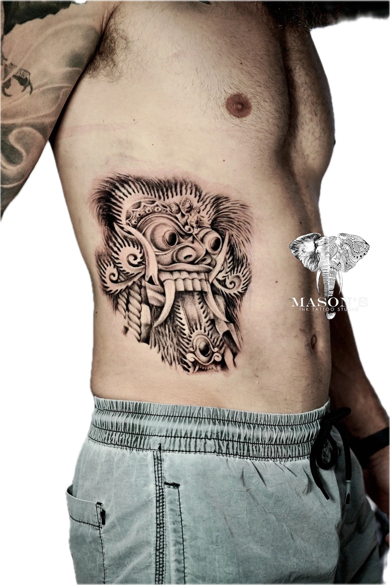 Balinese Barong Tattoo Design: a large black and grey mythological mask tattoo on the stomach