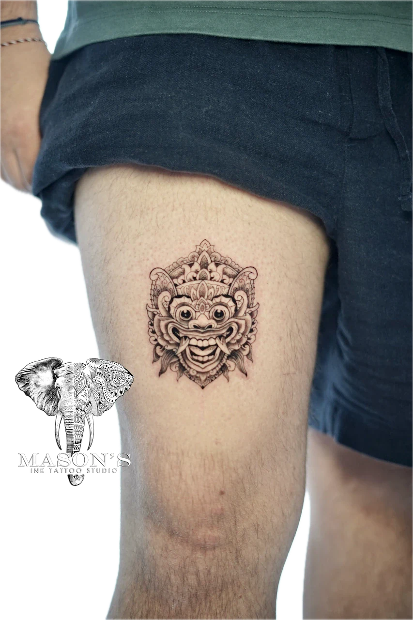 Traditional Barong Tattoo Design: a detailed demon face tattoo with ornamental flames on the thigh