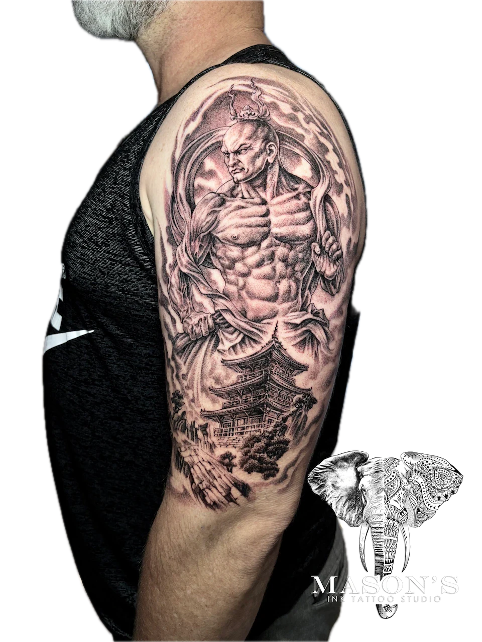 Black and Grey Monk Warrior Tattoo by Mason’s Ink: a muscular mythological figure with a temple and clouds on the upper arm