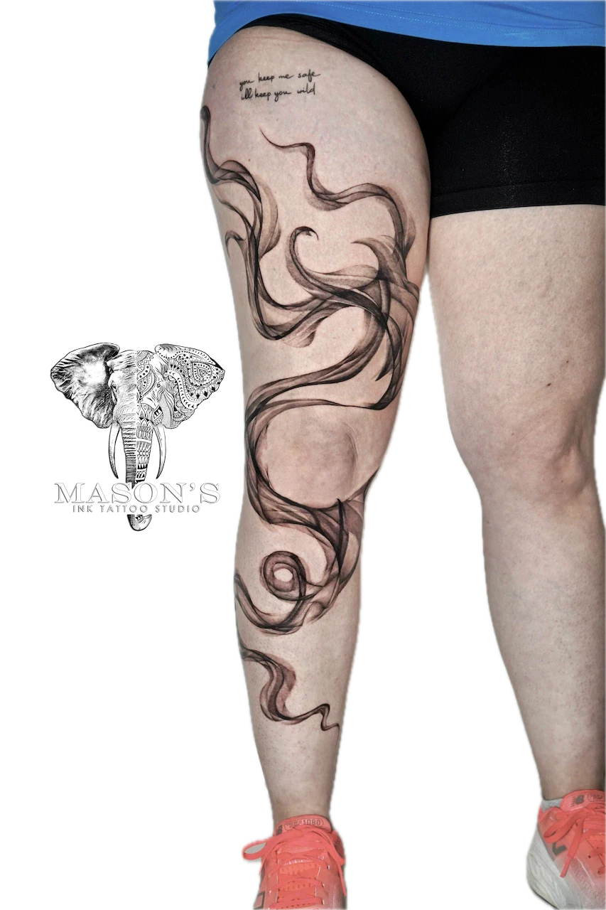 Black and Grey Smoke Tattoo Design: Intricate swirls and lettering on the thigh
