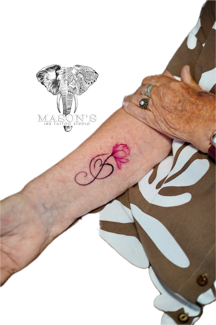Fine Line Color Floral Tattoo Design: a small pink flower with a letter and stem on the wrist