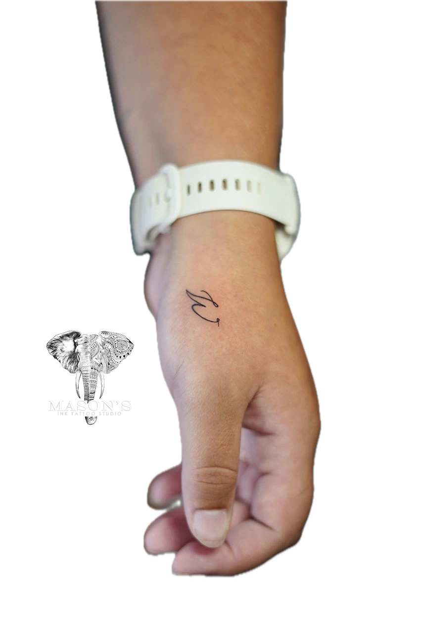 Fine Line Script Tattoo Design: a small black and grey cursive letter on the wrist