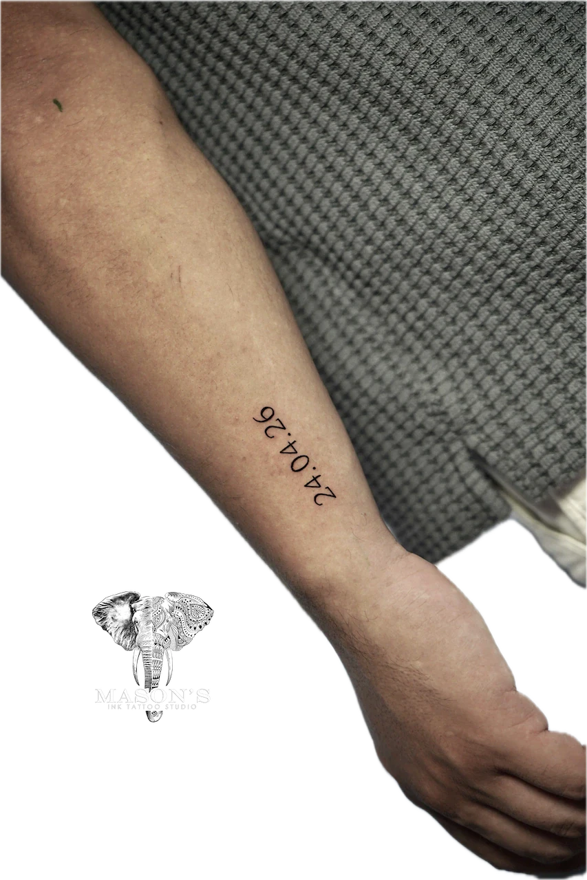 Fine Line Script Tattoo Design: a small black and grey date tattoo on the forearm