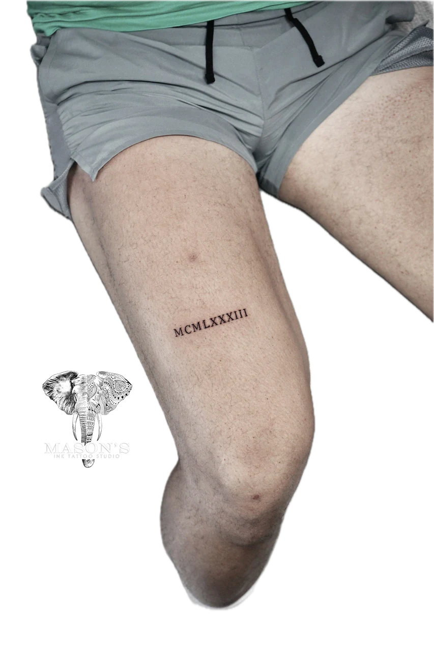 Fine Line Script Tattoo Design: Roman numeral lettering tattoo on the thigh