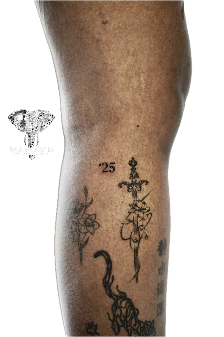 Fine Line Script Tattoo: a sword and flower tattoo with lettering and flames on a calf