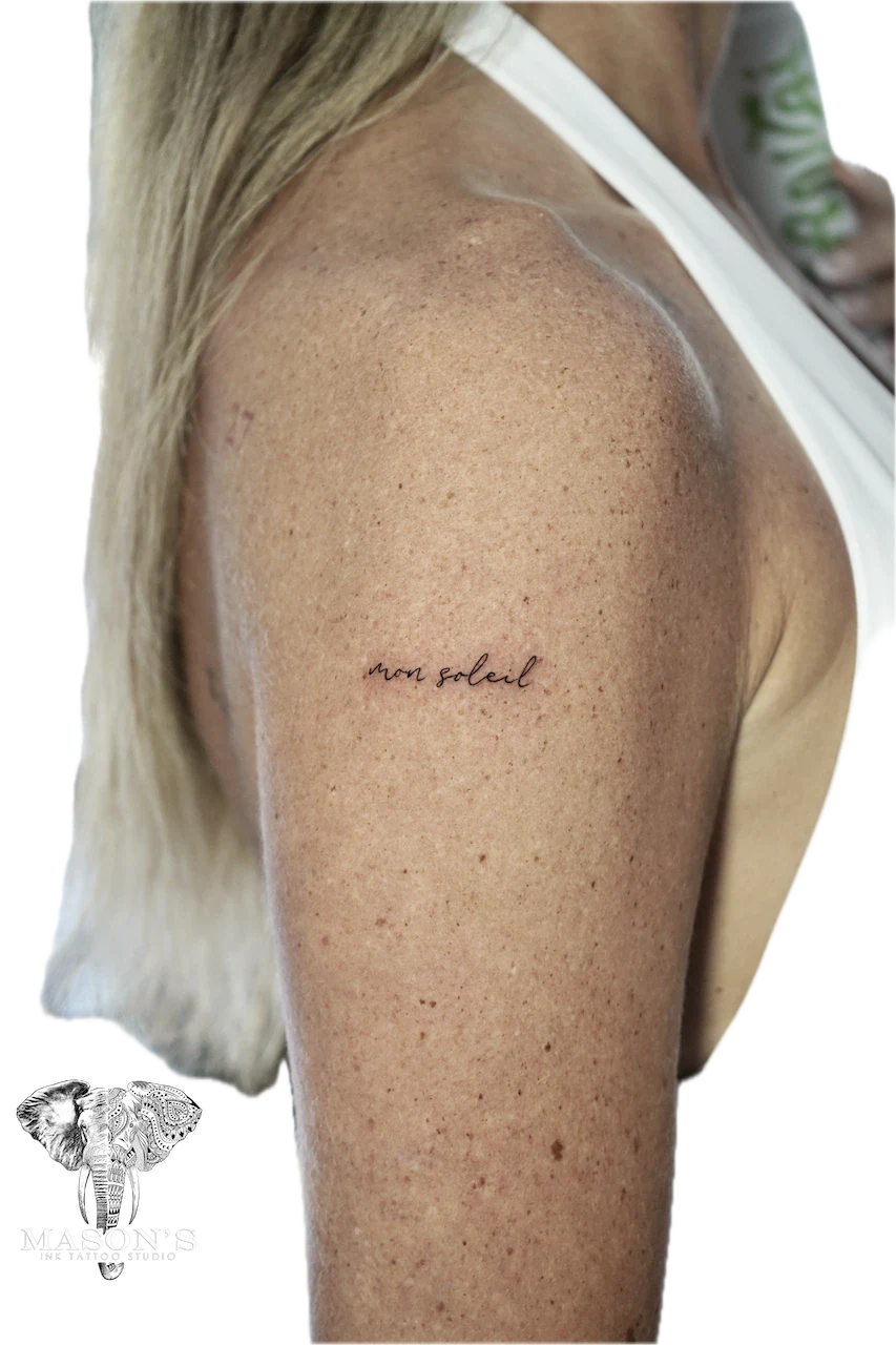 Fine Line Script Tattoo Design: Small black and grey lettering on the upper arm