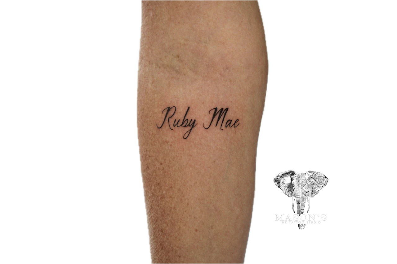 Fine Line Script Arm Tattoo Design: a memorial lettering tattoo on a calf