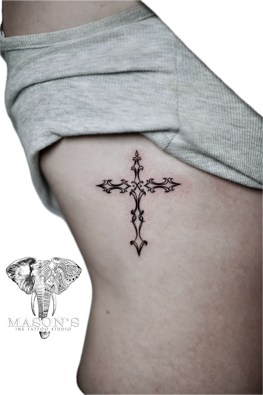 Fine Line Cross Tattoo Design: a small, ornate cross tattoo on the hip