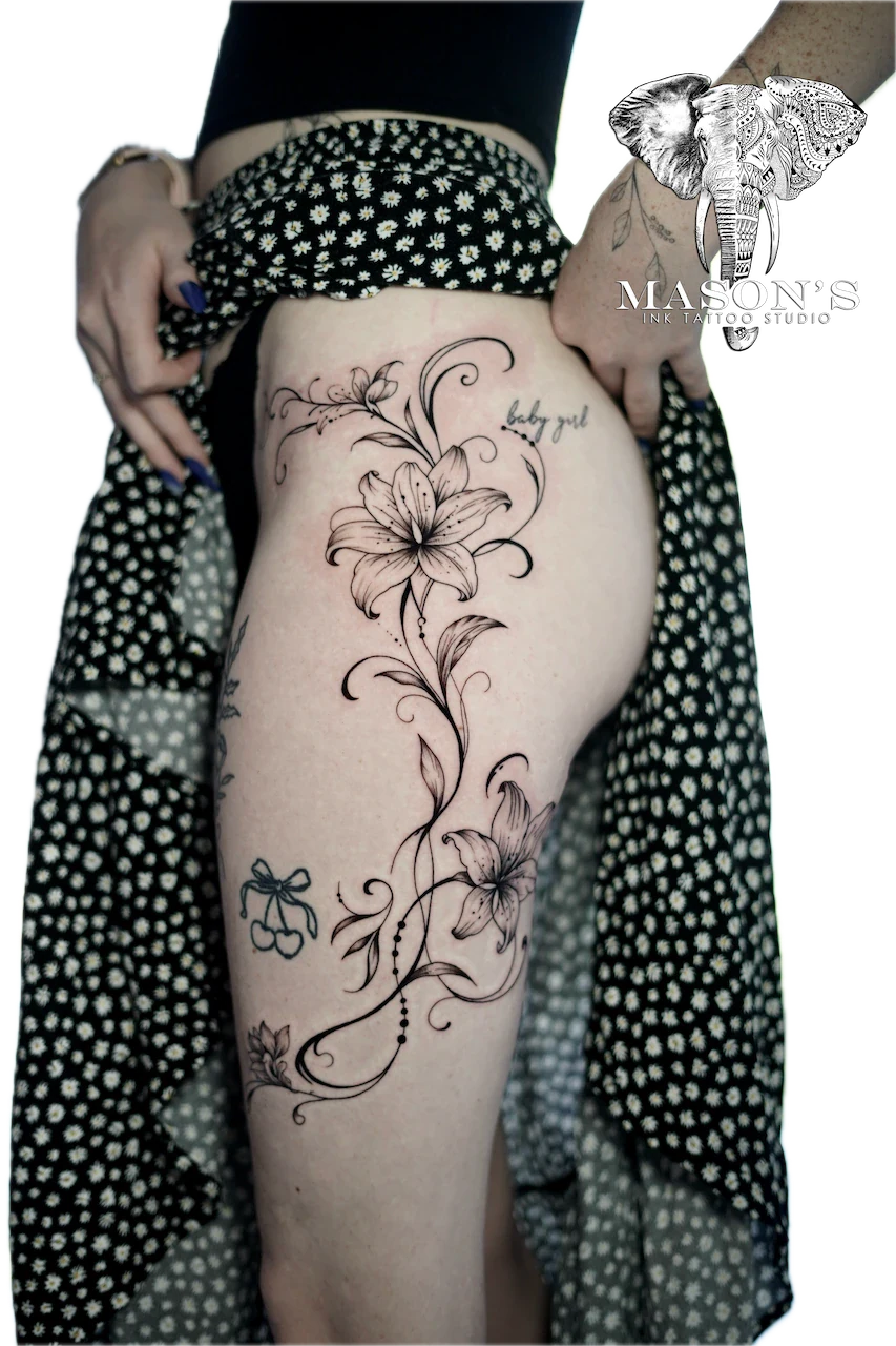 Fine Line Floral Tattoo Design: a large floral vine with a bow and lettering on the thigh