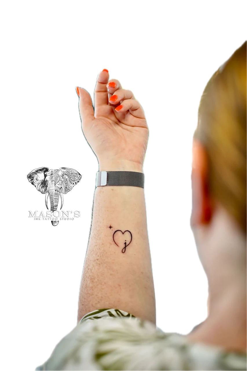 Fine Line Love Tattoo Design: a small heart with a letter and plus sign inside on the forearm