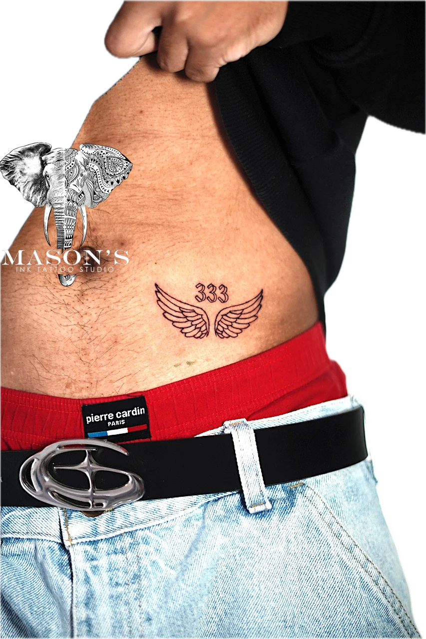Fine Line Wings and Script Tattoo Design: Minimalist wings with numbers tattoo on the stomach