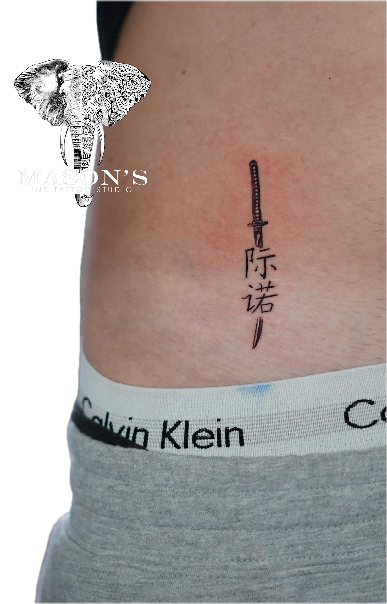 Japanese Fine Line Tattoo Design: a small Japanese sword with kanji lettering on the stomach
