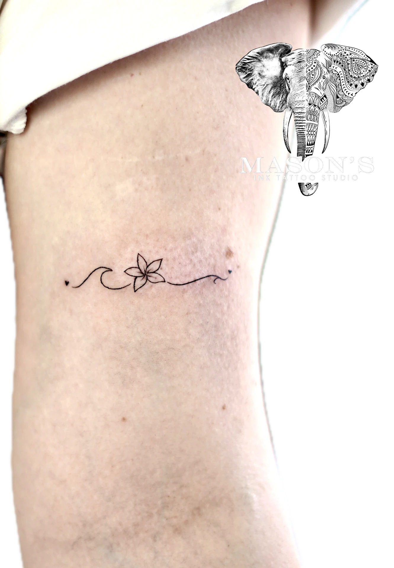 Floral Fine Line Tattoo Design: a minimalist tattoo of a flower and wave on the rib
